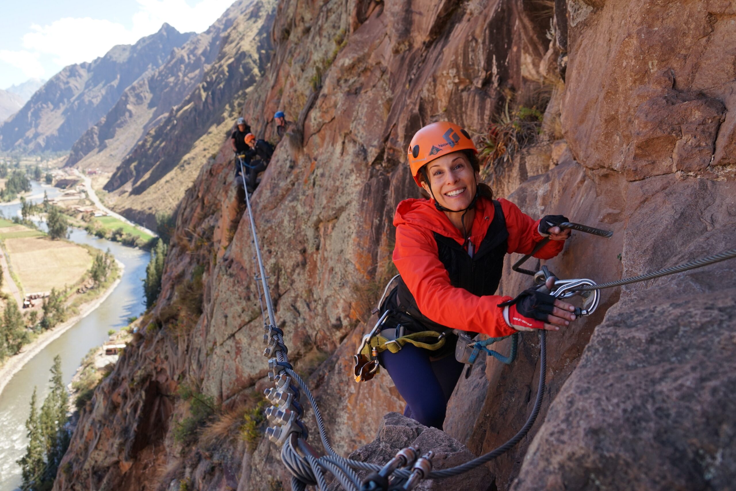 A woman smiling while safely climbing the Via Ferrata route, the secure steel cable and iron rungs visible, on her way to Skylodge.