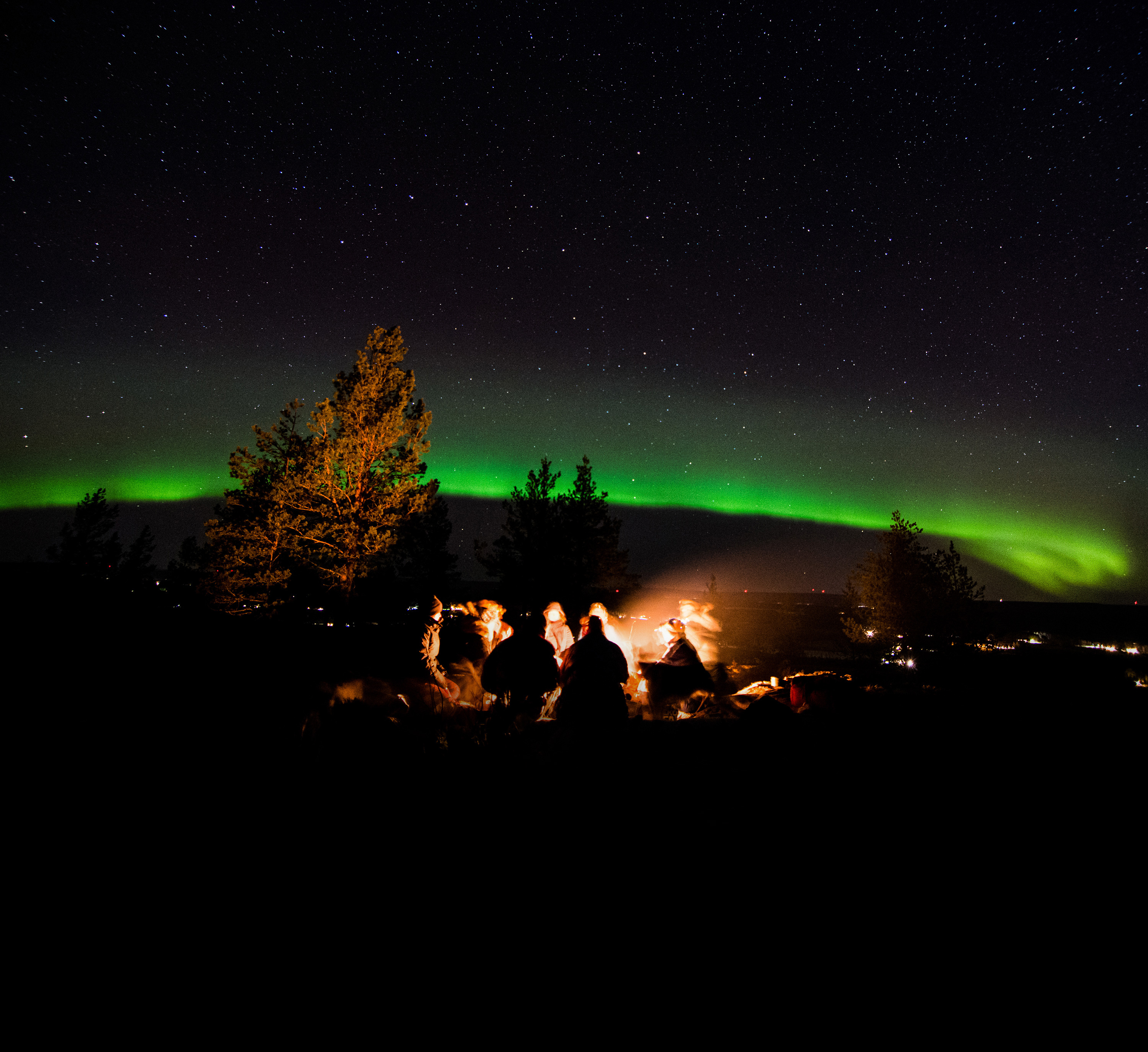 Guests gathering around a bonfire during a Northern Lights hunting tour with Treehotel under the starry Arctic sky.