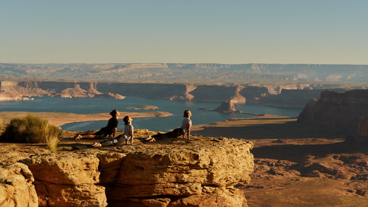 A group practices sunrise yoga on top of Tower Butte at Amangiri, with panoramic views of the Utah desert and Lake Powell below.