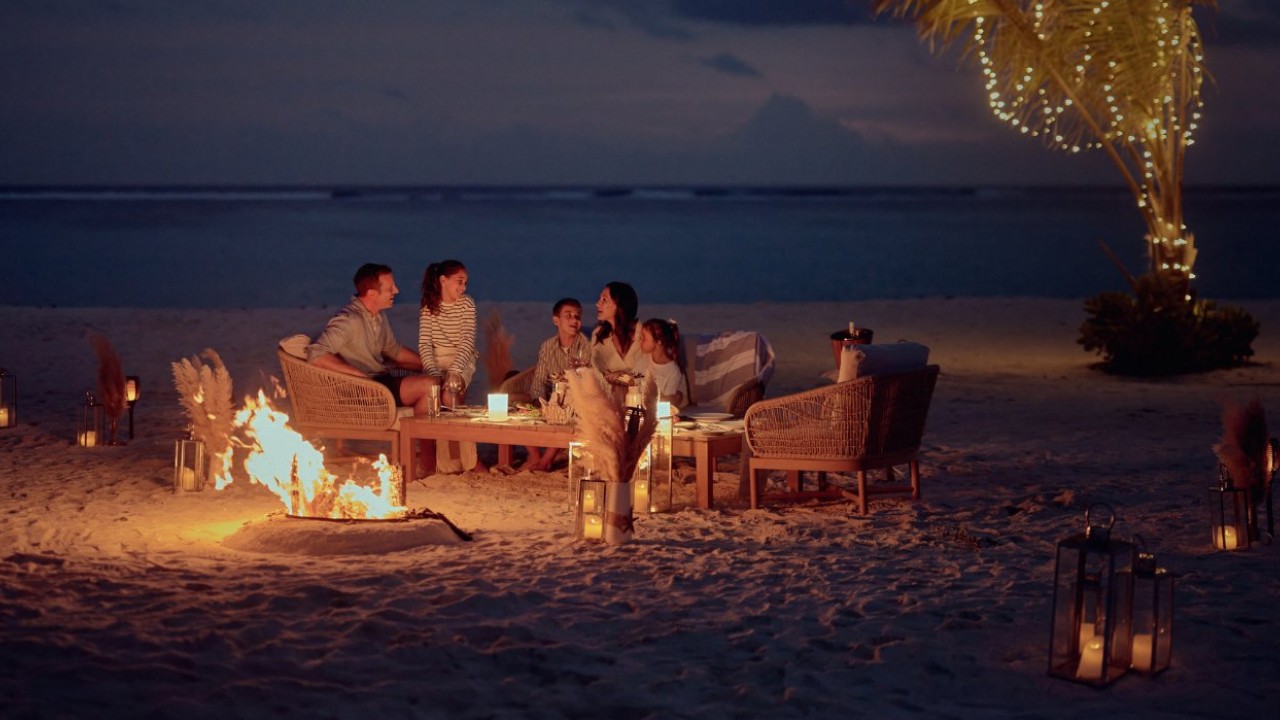 A family creates unforgettable memories around a private beach bonfire at sunset on the shores of Conrad Maldives Rangali Island.
