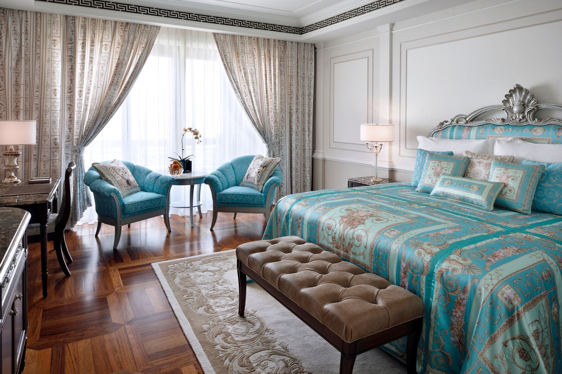 The comfortable bed and seating area in a Premier Versace Room with Dubai Creek views.