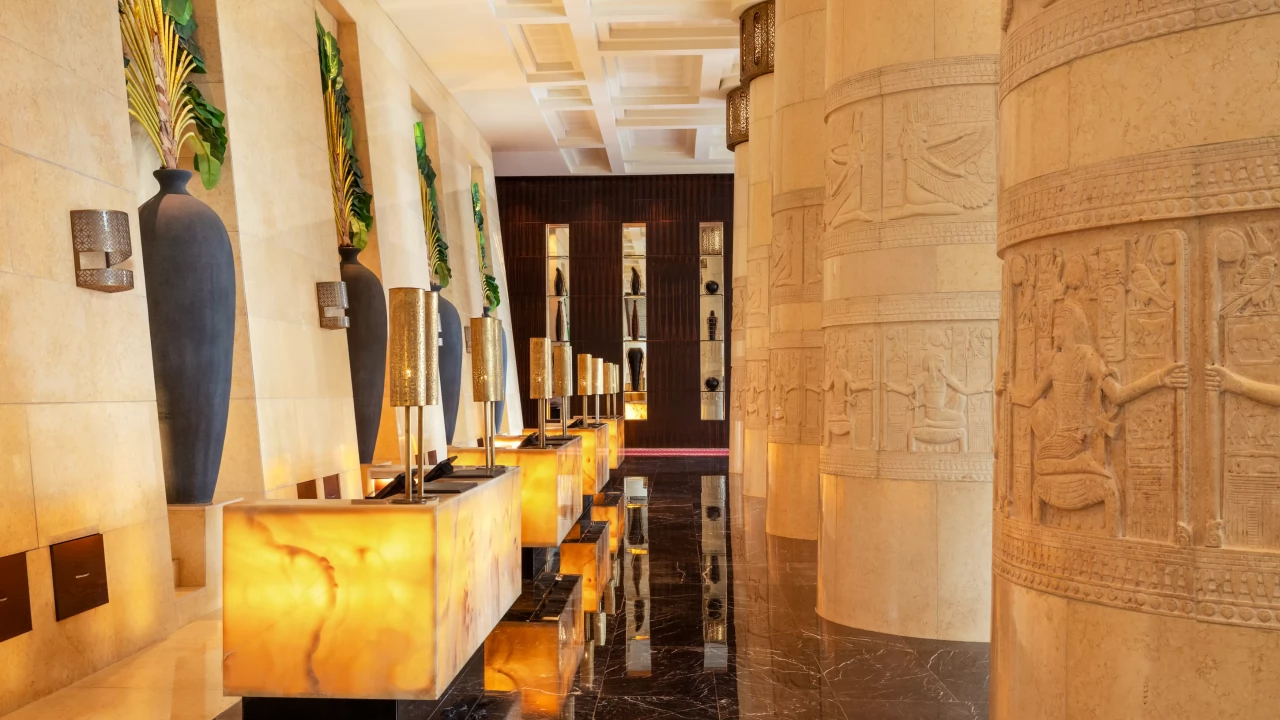 The majestic lobby of Raffles Dubai, featuring grand columns with intricate Egyptian hieroglyphics.