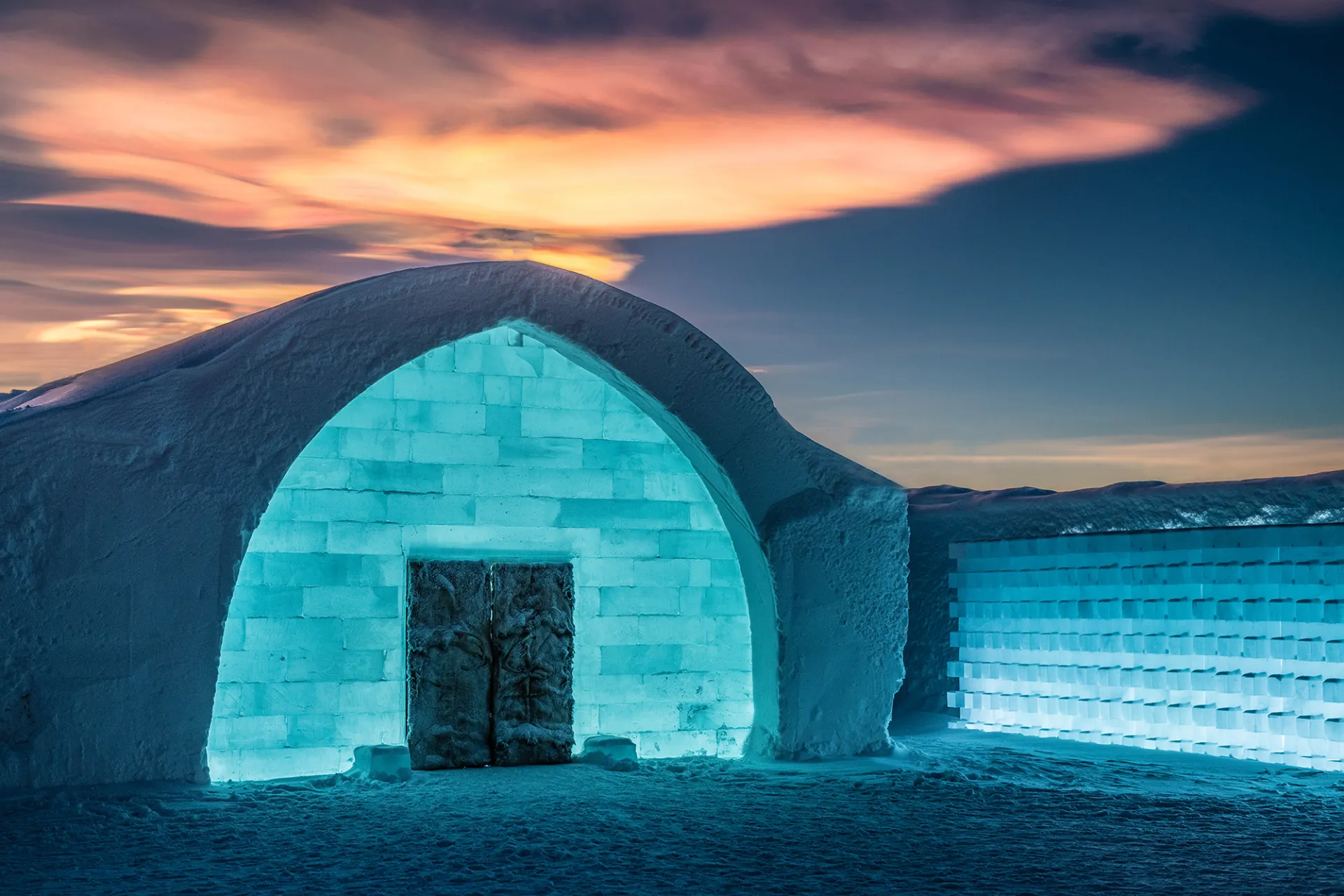 The majestic entrance of Icehotel in Jukkasjärvi, illuminated by the soft glow of an Arctic winter sunset.