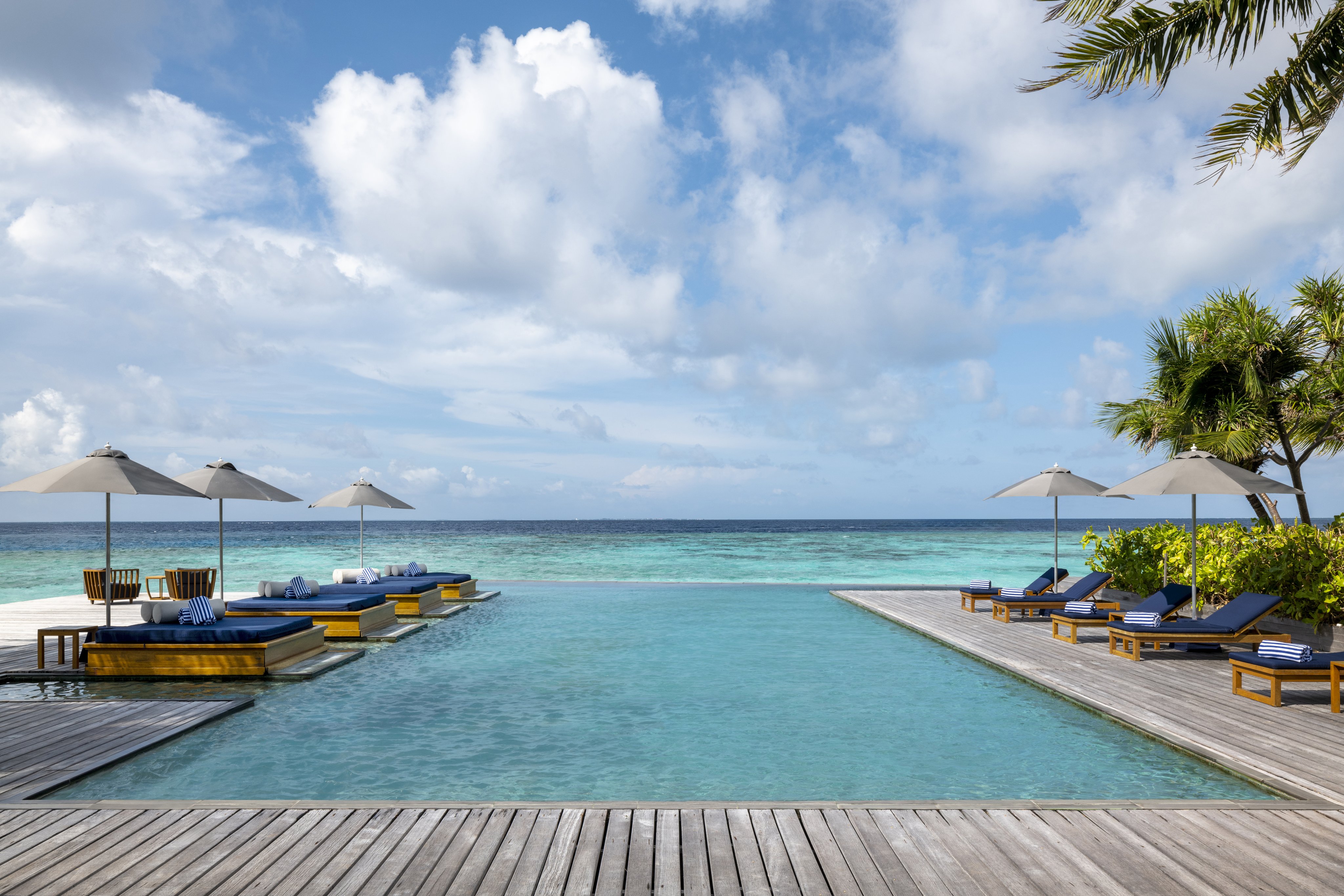 The main infinity pool overlooking the turquoise lagoon and ocean at The Halcyon Private Isles Maldives, with luxurious sun loungers and tropical landscaping.