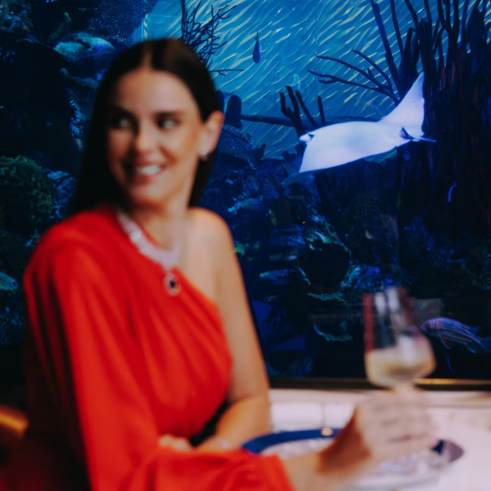 Guests dining at Al Mahara restaurant beside the floor-to-ceiling aquarium filled with exotic marine life, creating an immersive underwater experience at Burj Al Arab.